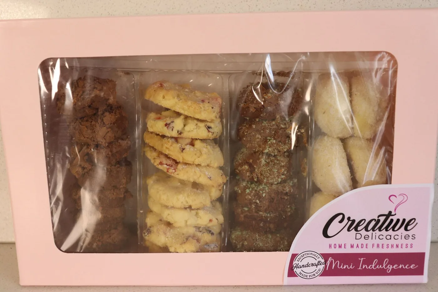 A pink Mini Indulgence box with four rows of handmade biscuits: chocolate, cranberry, mint chocolate and coconut
